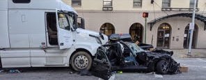 A white truck cab stopped in the street beside a car crushed down to its frame