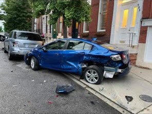 A blue car with its rear end torn open, folded into parked cars on a residential block