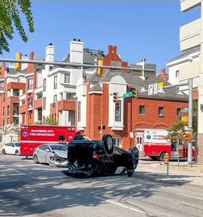 A black SUV upside down at an intersection, with two Baltimore City Fire Department medic units nearby