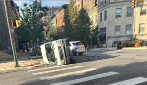 A white van lying on its side across a crosswalk at an intersection, with a damaged silver SUV behind it