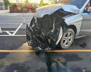A silver SUV with its front end torn off, with debris across the street